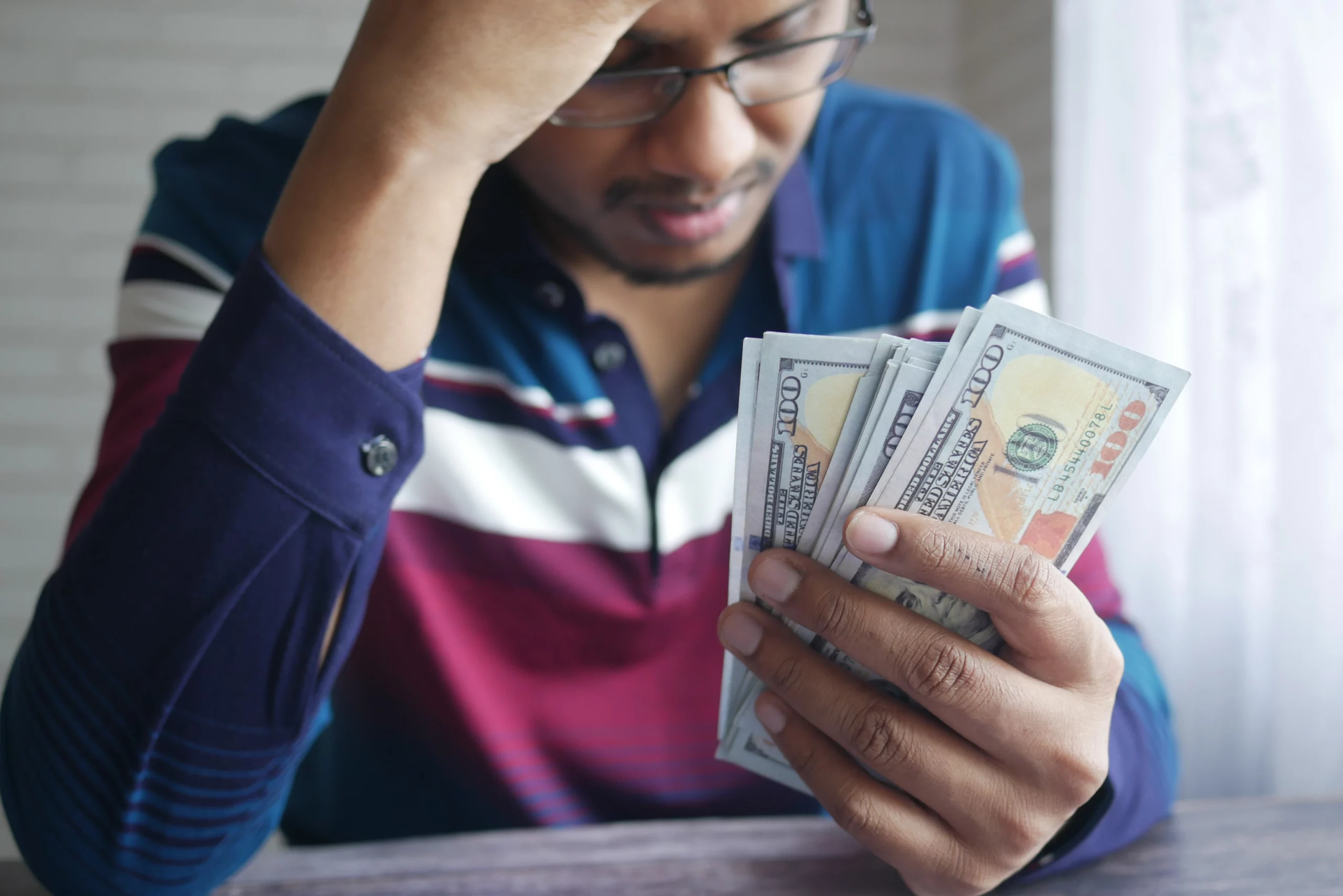 Person in striped shirt holding multiple $100 bills, looking stressed at a table—visualizing financial strain before considering bankruptcy options