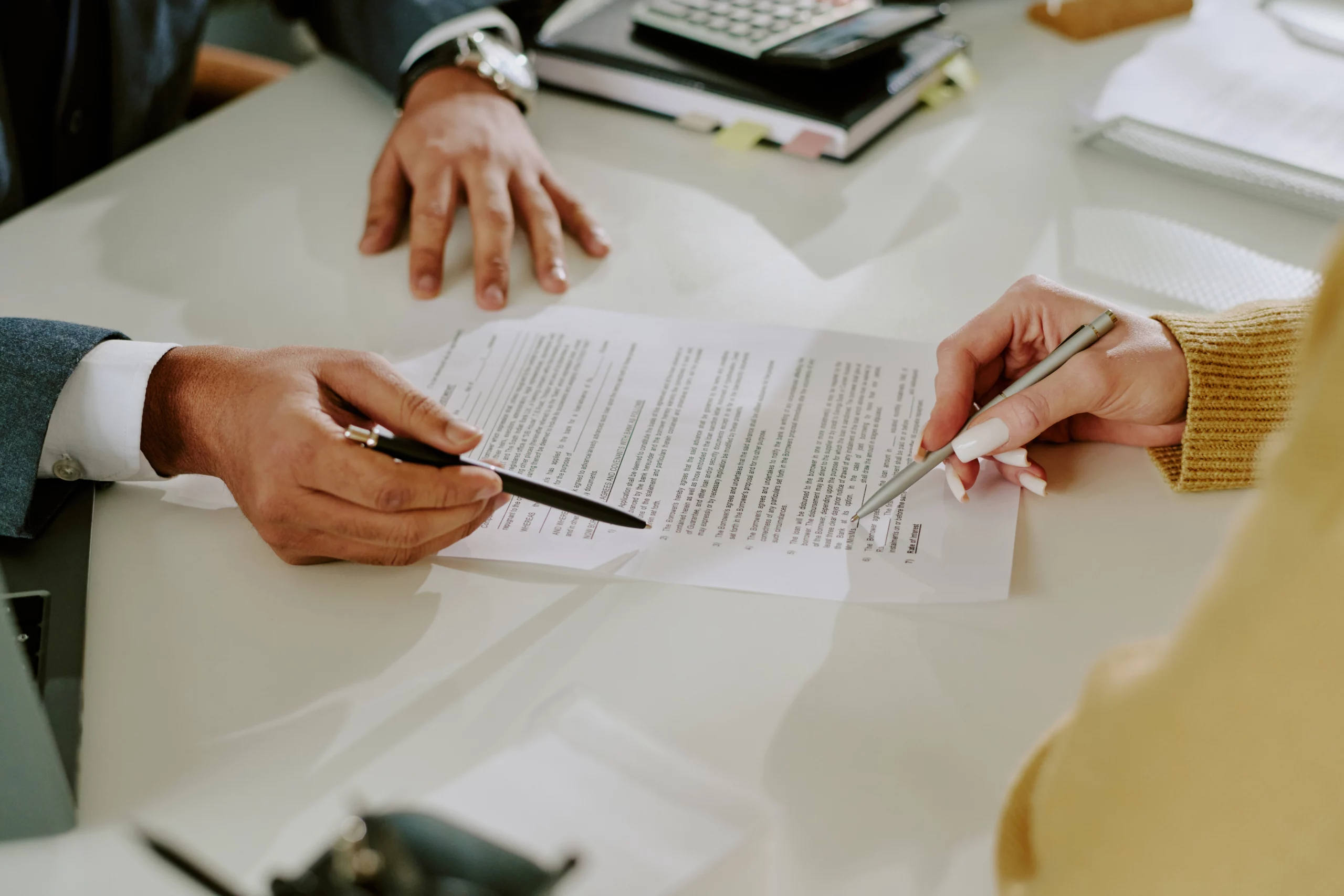 Two people reviewing a co-signed loan contract at a desk, ready to sign during a bankruptcy discussion.