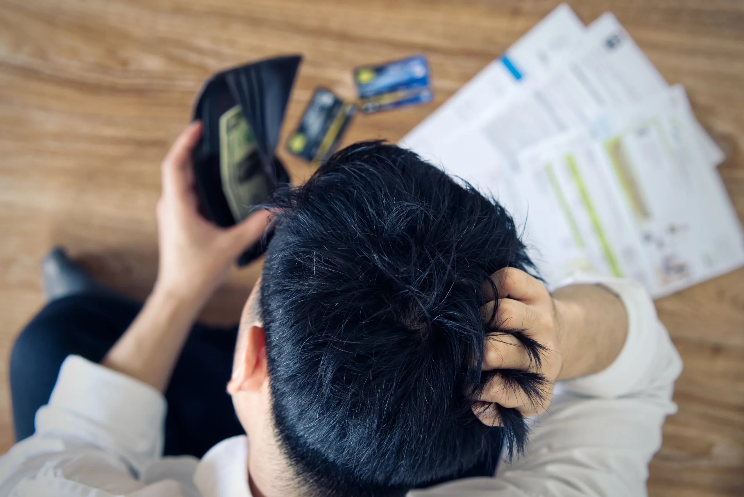 Person holding open wallet with few bills surrounded by credit cards and bills on wooden table, illustrating year-end financial stress and the decision to consider bankruptcy relief for overwhelming debt.