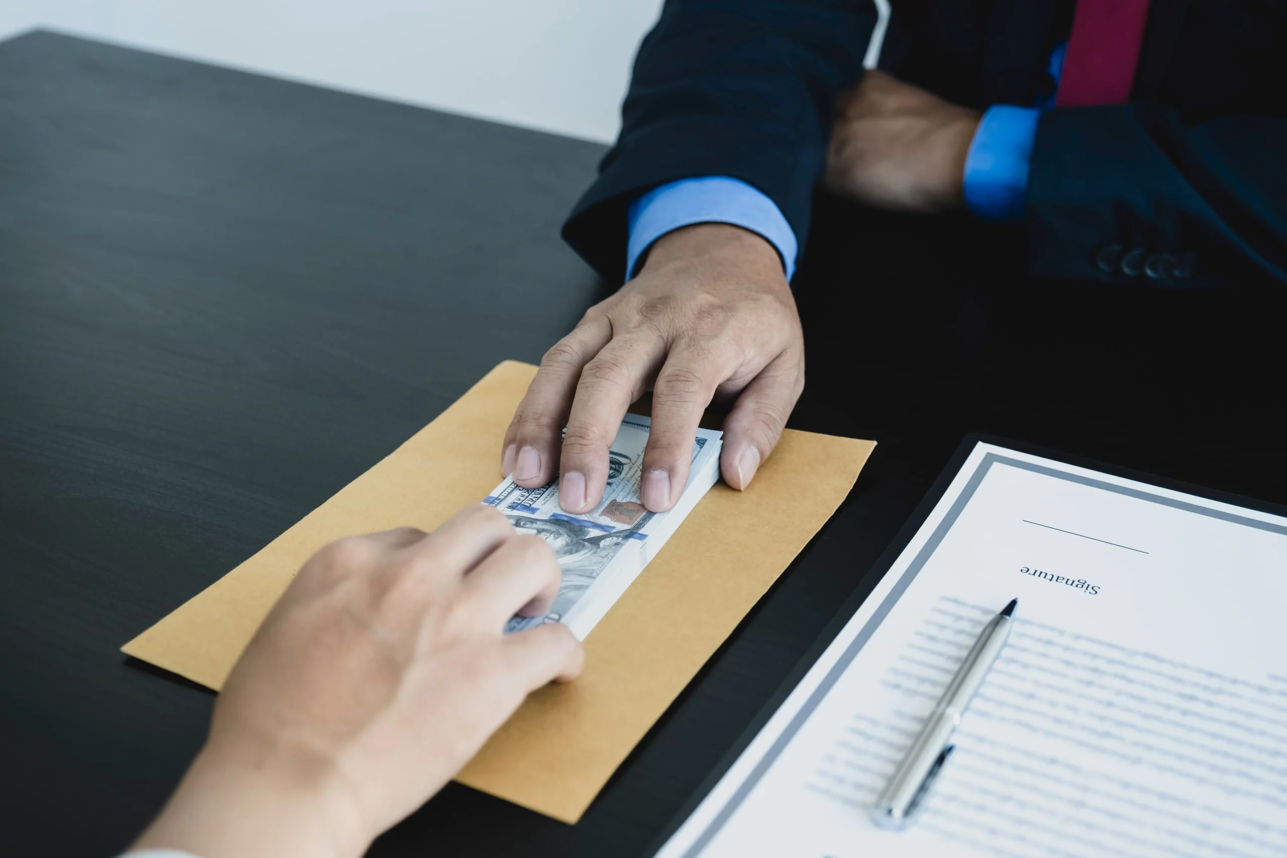 Two hands exchanging cash over a brown envelope on a desk illustrating potential loss of settlement money when filing for bankruptcy.