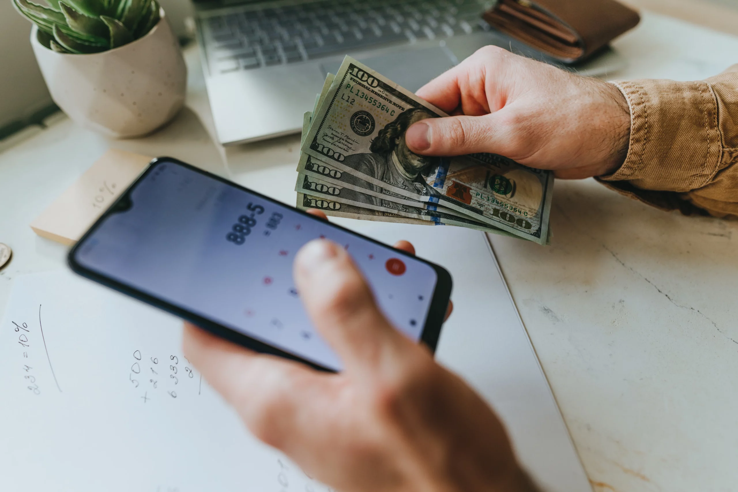 Person using a smartphone calculator while counting hundred-dollar bills, representing Cash App borrowing vs personal loans and financial planning before filing bankruptcy.