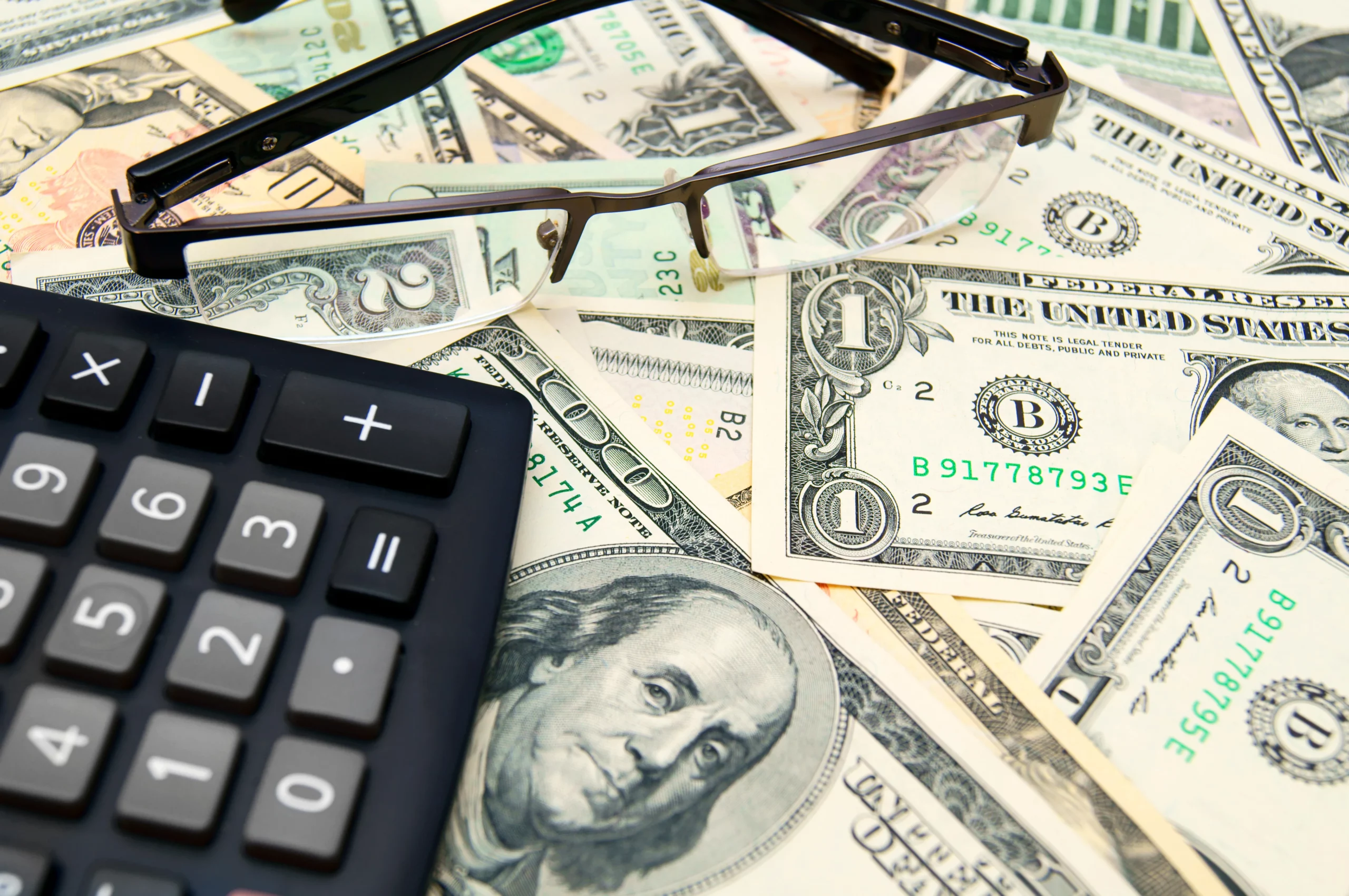 Calculator and eyeglasses placed on U.S. dollar bills, representing the financial considerations of receiving an inheritance during a Tennessee bankruptcy case.